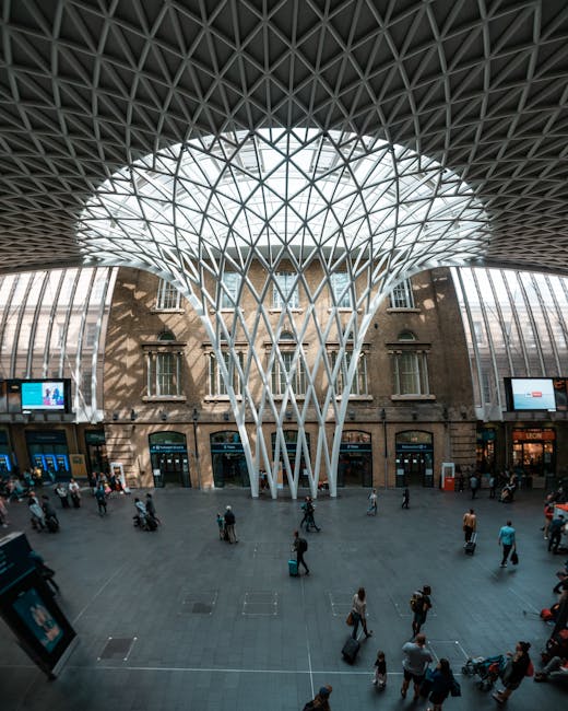 Interior view of Kings Cross station with a high, domed ceiling featuring a geometric lattice pattern made of metal and glass, allowing natural light to illuminate the bustling platform. The spacious 